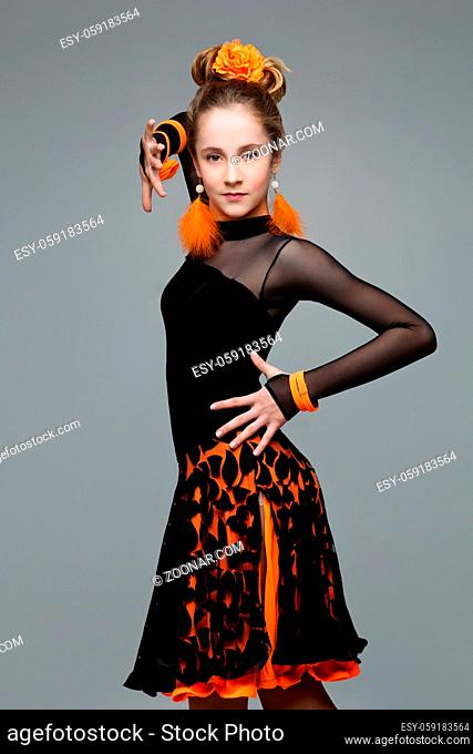 Beautiful teenage ballroom dancer girl in black and orange latina dress And accessories. Studio portrait on grey background. Copy space