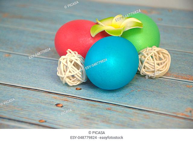 Three Easter eggs with decorative balls and a flower lie on a wooden table. Close-up