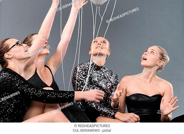 Young women with strings tied to balloon, grey background