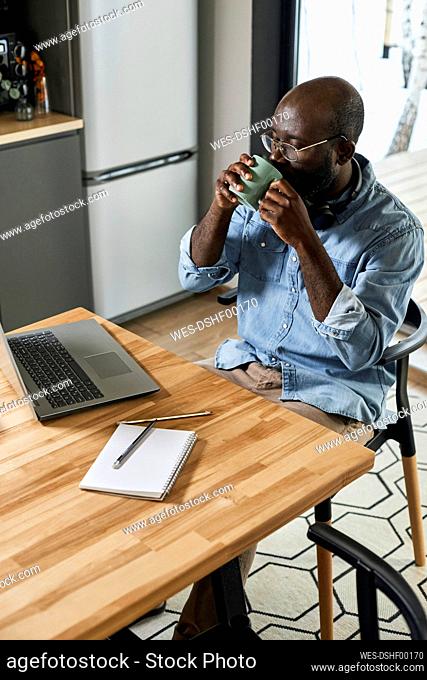Businessman drinking tea looking at laptop on dining table at home