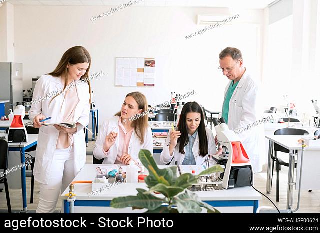 Students and teacher in white coats discussing in science class