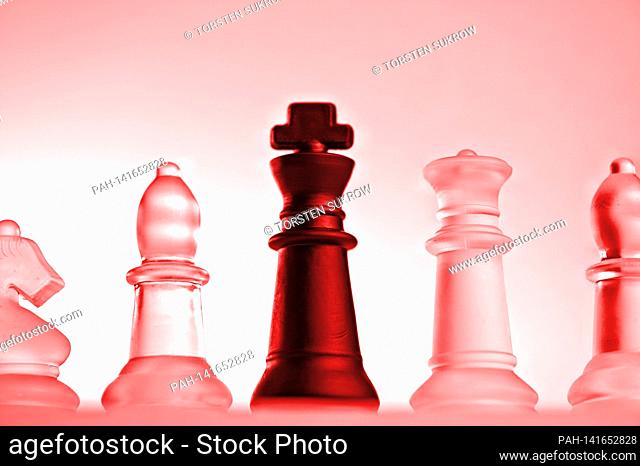 Symbolic chess pieces of a chess game made of glass with a neutral background. Detail of some white figures and the black king with a red light mood from a...