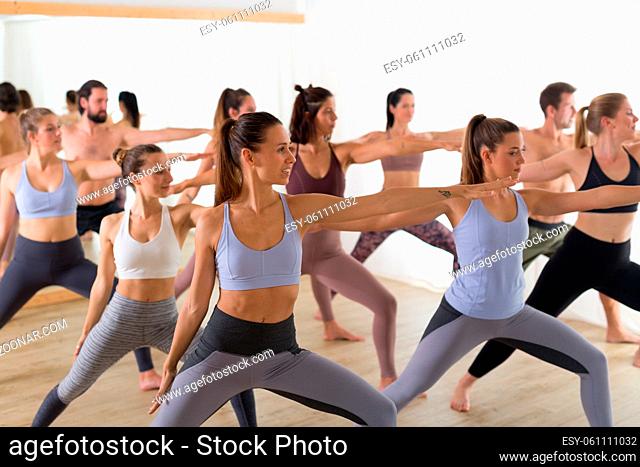 Group of young authentic sporty attractive people in yoga studio, practicing yoga lesson with instructor. Healthy active lifestyle, working out in gym