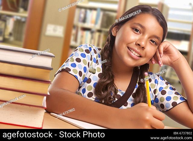 Happy hispanic girl student with pencil and books studying in library