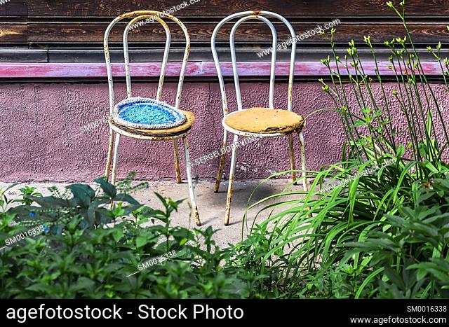 Two old metal chairs stand against the wall of a residential building close