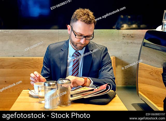Handsome businessman with striped tie sits at table with coffee reading a newspaper or magazine