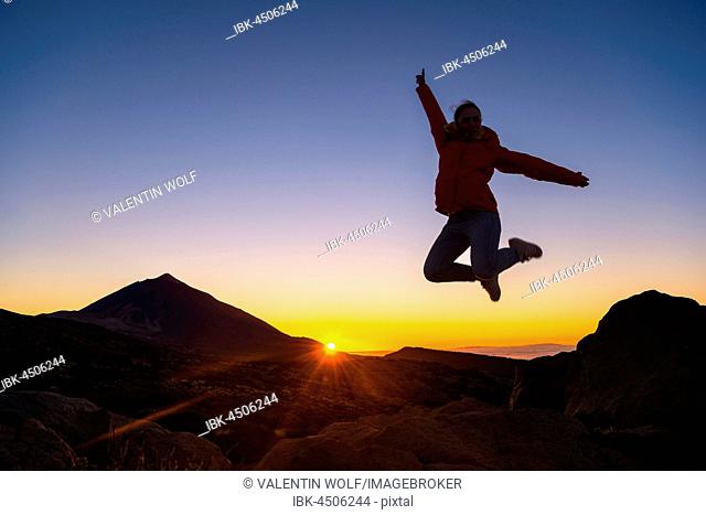 Young woman jumping in the air, on rocks, joy, Sunset, Volcano Teide and volcanic backlit scenery, Silhouette, National Park El Teide, Tenerife, Canary Islands