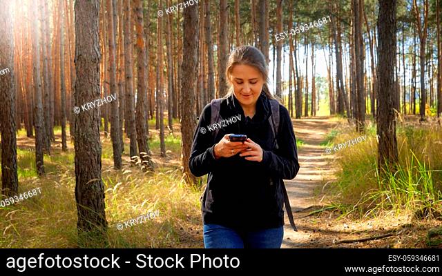 Portrait of beautiful smiling female tourist walking on hiking route and using navigator in smartphone