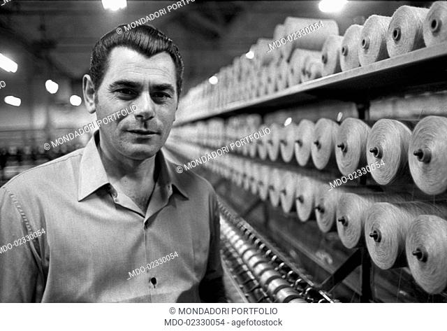 Portrait of a workman beside the spinning machine of a woolen mill. Italy, 1968