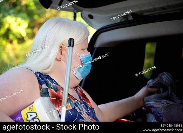 Albino woman grabbing groceries from the back of a car while wearing a medical mask