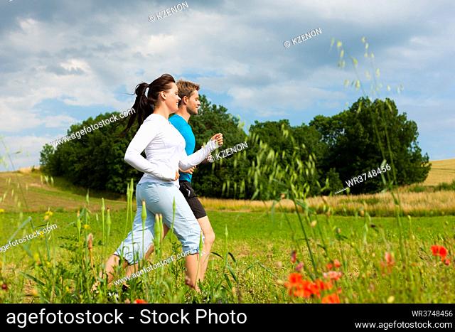 Young fitness couple doing sports outdoors, jogging on a green meadow in summer under a blue sky