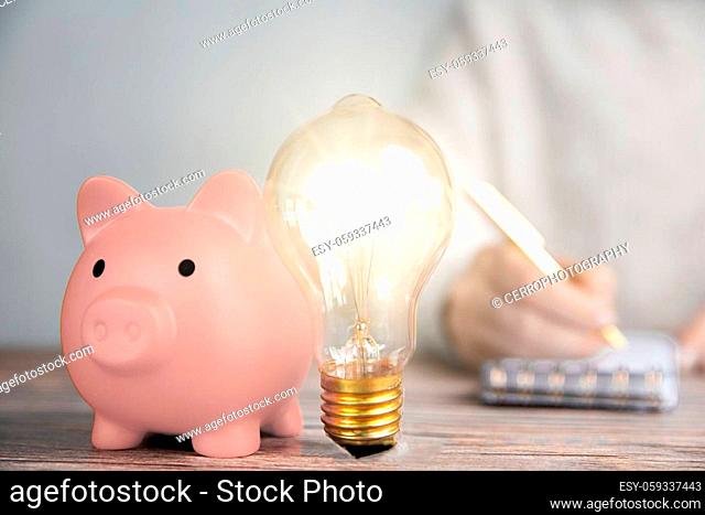 Shining lightbulb and pink piggy bank, business person writing Financial ideas, creative savings, investment budget concept copy space closeup
