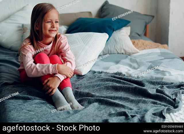 Positive little girl sitting on bed