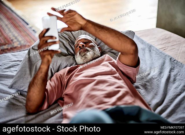 Man using mobile phone lying on bed at home