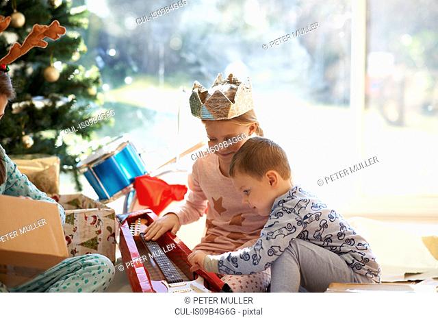 Girl and brother on living room floor looking at toy guitar christmas gift