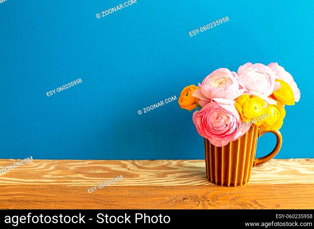 Vase of ranunculus flowers on wooden table. blue background