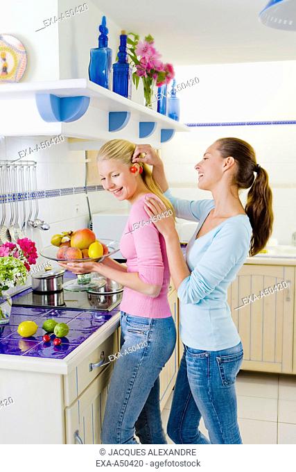Two young girls smiling and having fun while fooling around in the kitchen