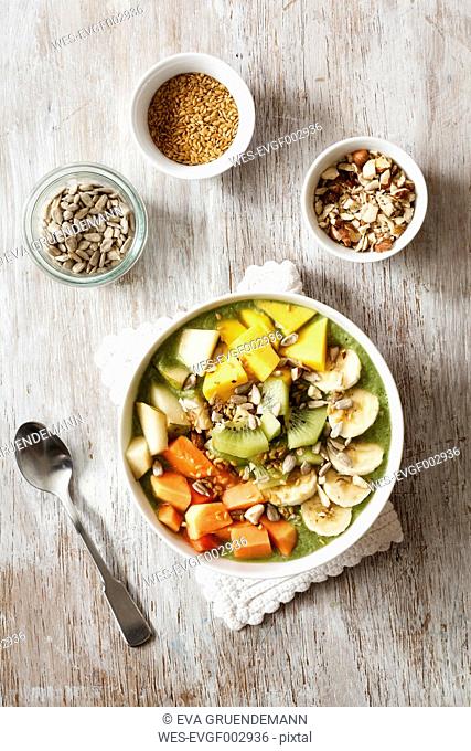Smoothie bowl with different fruits, mango, papaya, kiwi, banana and pear and toppings, lineseeds, sunflower-seeds and nuts