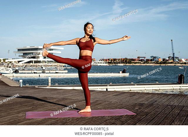 Asian woman practicing yoga, standing on one leg, hand-to-big-toe pose
