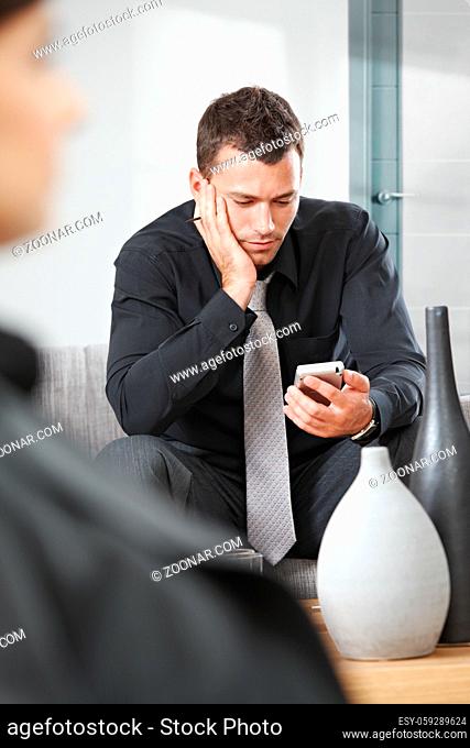 Young businessman sitting on sofa at office lobby using palmtop organizer