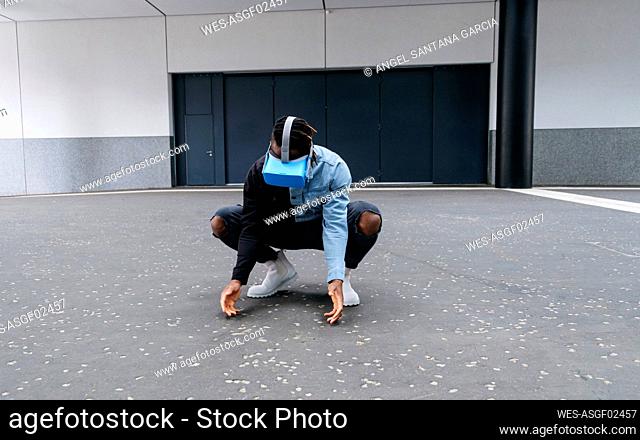 Young man crouching on road wearing virtual reality headset