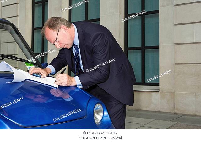 Man signing document on car bonnet