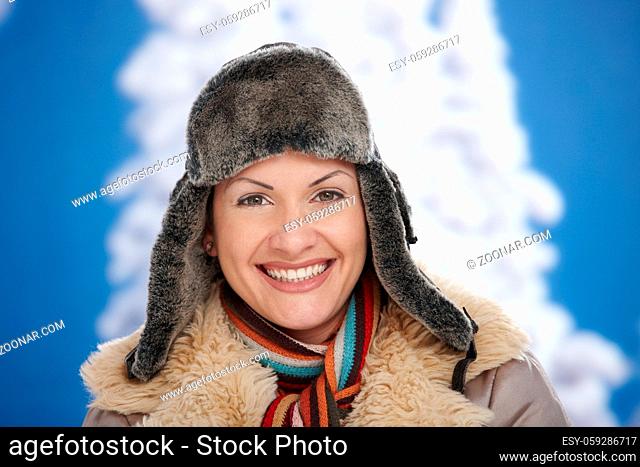 Happy young woman in snow at winter wearing warm clothes, looking at camera, smiling