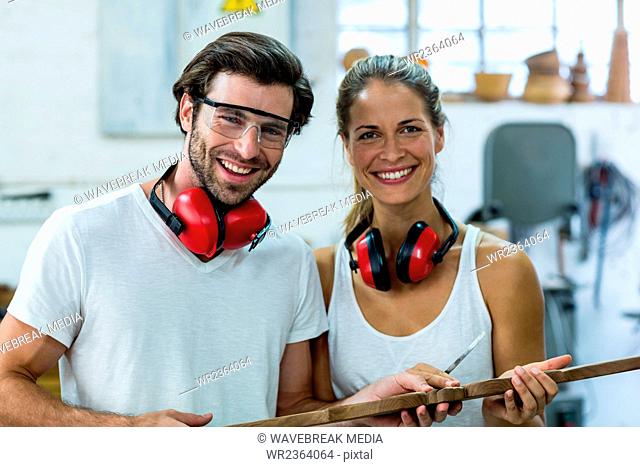 Male and female carpenters standing together with wooden plank