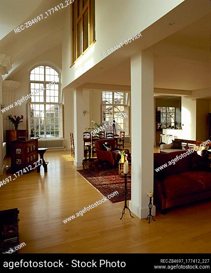 Open plan living and dining area with wood floor, arched windows and columns