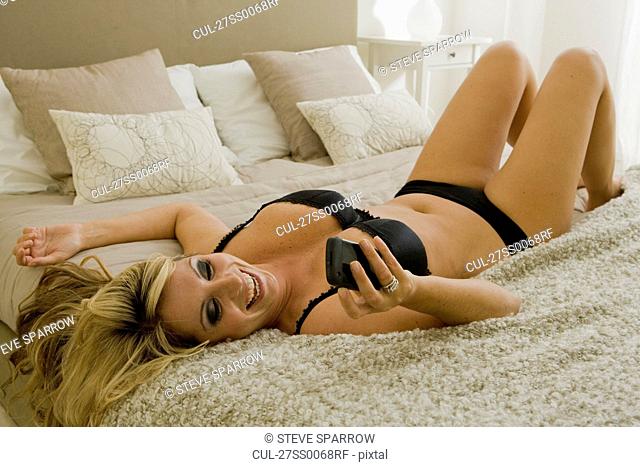 Busty young woman on bed with cell phone