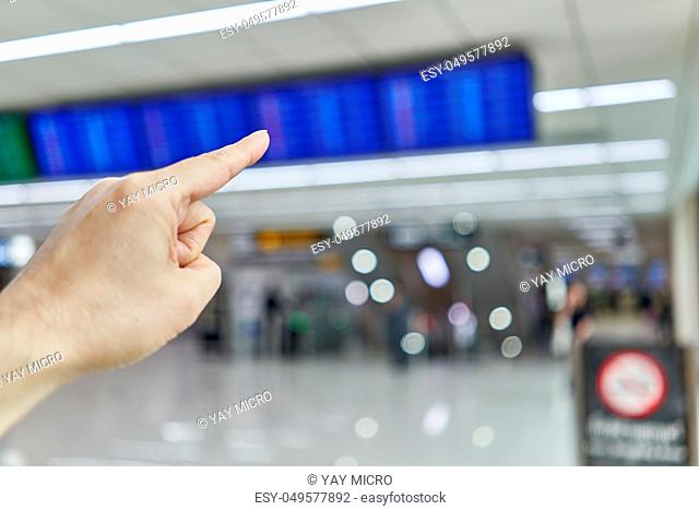 Finger of man is pointing at blur flight schedule for check timetable to departure in non smoking area at international airport terminal with copy space