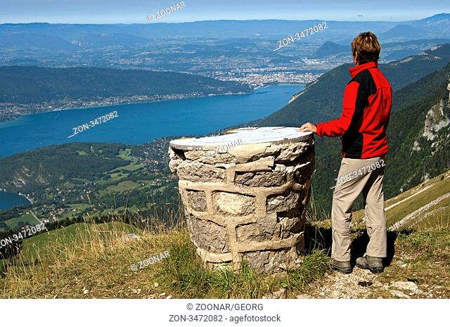 Wanderer steht an einer Orientierungstafel nahe der Tournette Schutzhütte im Bergmassiv Bornes Massif des Bornes und blickt über dem See von Annecy Lac d'Annecy...