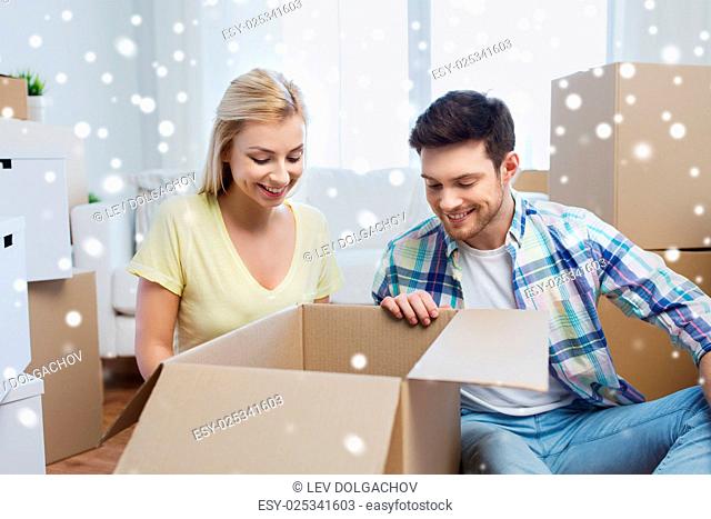 moving, people, repair and real estate concept - smiling couple looking into big cardboard box at new home over snow