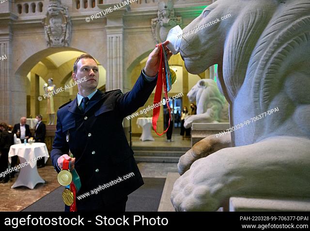 28 March 2022, Saxony, Dresden: Francesco Friedrich, four-time Olympic bobsleigh champion, places his FFP2 mask on the nose of a sandstone lion statue for a...