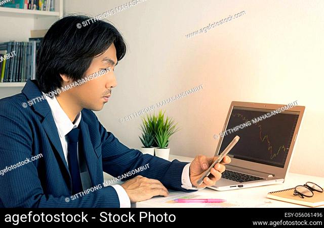 Young Asian Forex Trader or Investor or Businessman in Suit Looking Smartphone and Trading Forex or Stock Chart by Laptop in Trader Room in Vintage Tone
