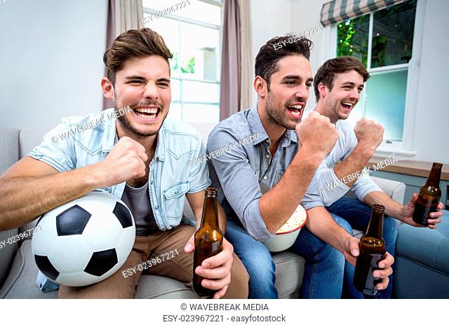 Cheerful male friends watching soccer match on TV