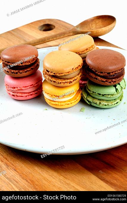 Colored macaroons on white plate on wooden board