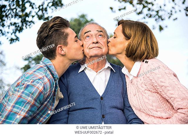 Grandson and daughter kissing senior man's cheek