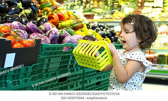 Child shopping eggplants in supermarket. Concept for buying fruits and vegetables in hypermarket. Little girl hold shopping basket