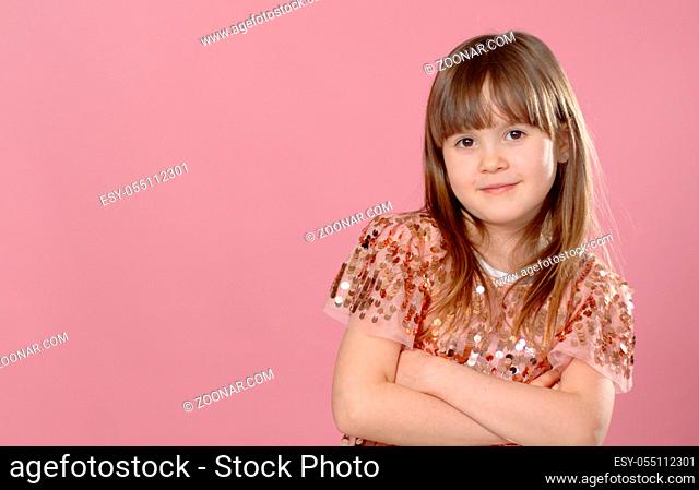 Close up shot of beautiful blonde Caucasian little girl wearing sequin dress, looking at the camera with adorable smile, posing against pink copy space...