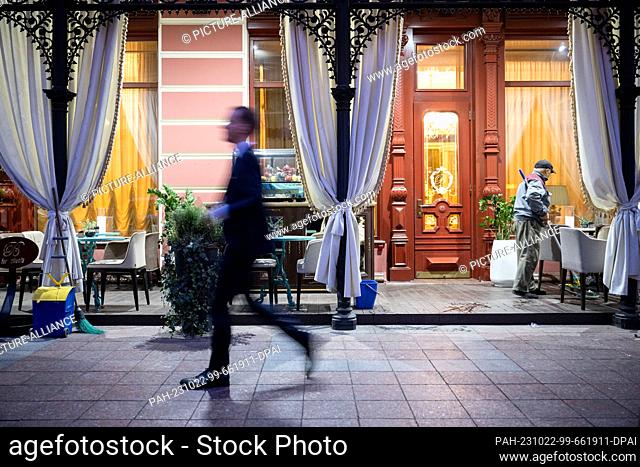 21 October 2023, Ukraine, Odessa: A man walks past a downtown hotel in the morning, on whose porch an employee is sweeping
