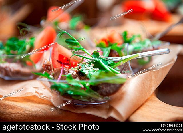 Tasty beef tongue meat with greens tomato sesame and sauce on a wooden board. Catering concept