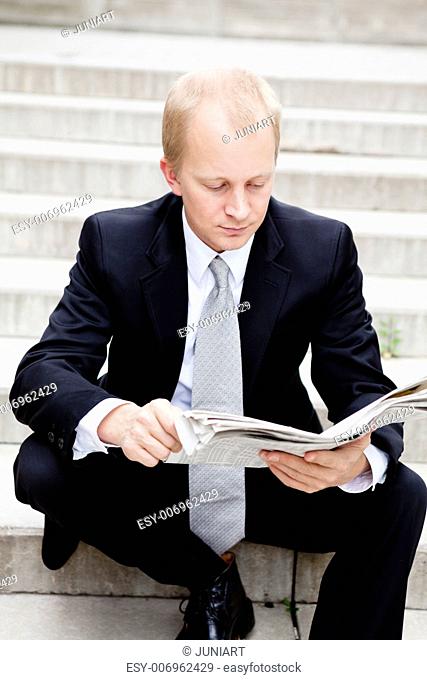 young business man is reading newspaper outdoor in summer