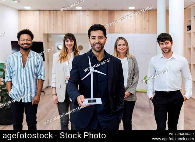 Businessman holding wind turbine model in front of his team in office
