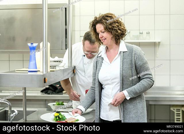 Service woman taking food from chef in restaurant or hotel kitchen