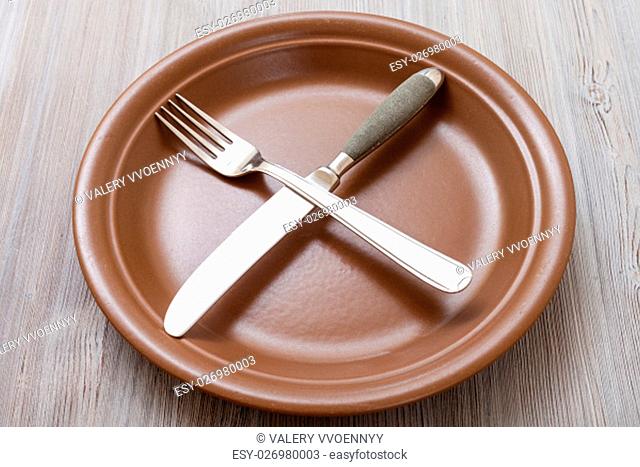 food concept - brown plate with crossing knife, spoon on gray brown table