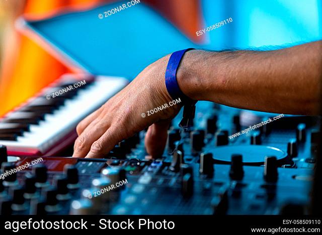 A close up selective focus shot from the side as a electronic dance music, EDM, DJ performs on stage, using hand to control modern mixing equipment