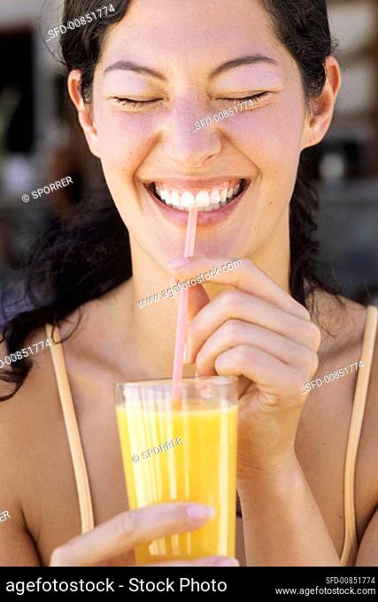 Young woman drinking orange juice through a straw