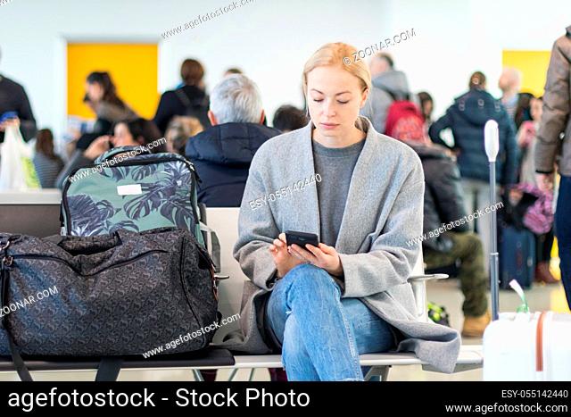 Casual blond young woman using her cell phone while waiting to board a plane at the departure gates at the airport terminal