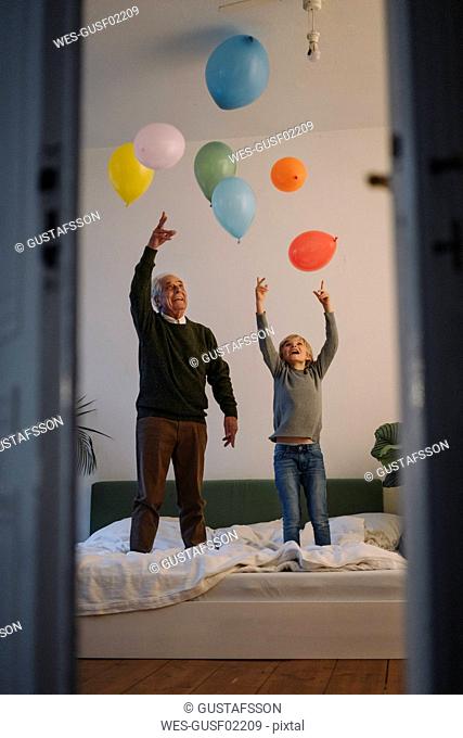 Happy grandfather and grandson playing with balloons on bed at home